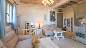 Amplia sala de estar con sofá, mesa de centro y candelabro. Zona de cocina con armarios y refrigerador.
