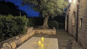 Un área de comedor al aire libre con una mesa y sillas de piedra, rodeada de muros de piedra y un árbol.