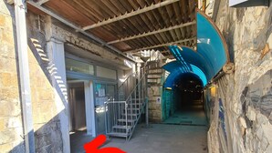 Un passage intérieur, avec un mur en pierre d’un côté et un escalier en métal menant à un niveau supérieur.
