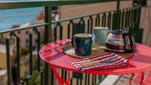 Une table rouge, sur laquelle se trouvent une tasse, un thermos et un torchon, est placée sur un balcon donnant sur la mer.