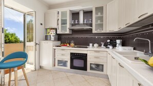 Een kleine keuken met witte kastjes, een magnetron, een fornuis en een spoelbak.