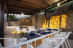 An outdoor dining area with a stone wall backdrop, a wooden ceiling, and a stone fireplace. - AMORE RENTALS -VILLA FELICE – with Private Pool, Garden and Sea View in the Sorrento Peninsula (Massa Lubrense)