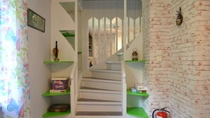 A staircase with green shelves on either side, a fire extinguisher on the right, and a floral curtain on the left. - Little Sweden, that's what we call the place where the house is located in the High Coast area. (Resele)