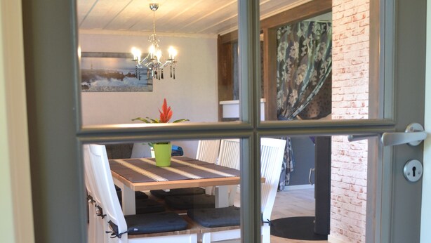 A dining area with a table and chairs, a chandelier, and a view through a glass door. - Little Sweden, that's what we call the place where the house is located in the High Coast area. (Resele)