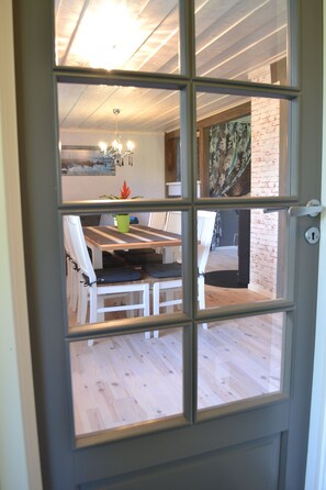 Un coin repas avec une table et des chaises, un lustre et une vue sur l’extérieur, visible à travers une porte vitrée.