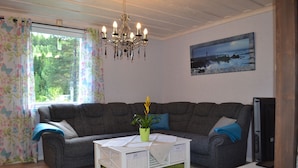 A living room with a grey sofa, a white coffee table, a green rug, and a chandelier. - Little Sweden, that's what we call the place where the house is located in the High Coast area. (Resele)