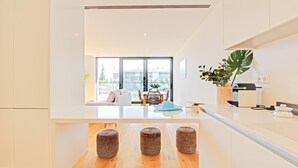 Une cuisine moderne dotée d’un îlot central, d’un coin repas avec une table et des chaises, et d’une grande fenêtre offrant une vue sur l’extérieur.