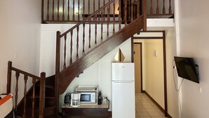 A wooden staircase leading to a second floor, a kitchen area with a microwave, toaster, and coffee maker, and a flat-screen TV mounted on the wall.