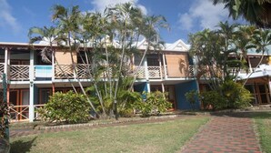A hotel with multiple floors, balconies, and tropical landscaping. - Mayero: Belfond Apartment (Sainte-Anne)