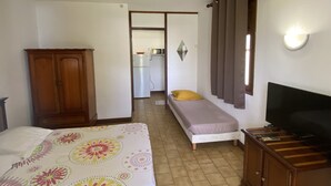 A bedroom with a bed, a wardrobe, a television, and a kitchenette in the background. - Mayero: Belfond Apartment (Sainte-Anne)
