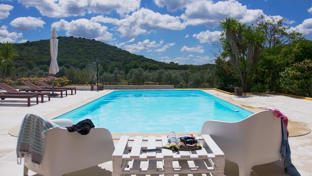 A poolside area with lounge chairs, a small table with towels and a hat, and a view of a mountain and trees. - (10PAX) Peace bellow a starred sky with special views to olives and cork tree (Evoramonte)