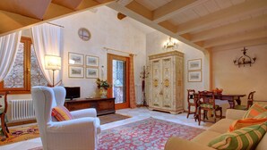 A cozy living room with a white armchair, a sofa, a dining table with chairs, a cabinet, and a large window with curtains. - MOCENIGO aperitif (Venezia)