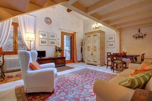 A cozy living room with a white armchair, a sofa, a dining table with chairs, a cabinet, and a large window with curtains. - MOCENIGO aperitif (Venezia)