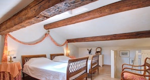 Ein Schlafzimmer mit einem Einzelbett, Holzbalken, einem Nachttisch, einem Stuhl und einem gemusterten Teppich.