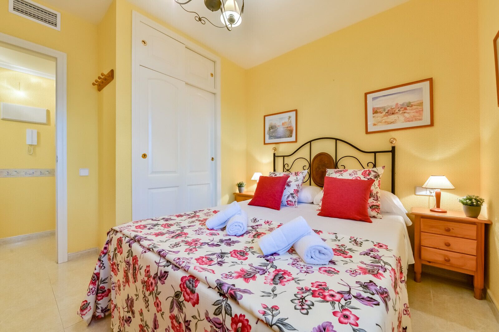 A hotel room with a bed, a nightstand, a lamp, a door, and a wall with a painting.