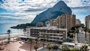 Paesaggio costiero con una montagna imponente, edifici moderni e una spiaggia.