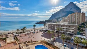 Un hotel sulla costa con piscina, accesso diretto alla spiaggia e montagne sullo sfondo.