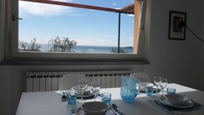 A dining table set for two with a view of the sea through a window. - Ulivi House: Parking, Pool, Tennis, 2 AC BDR, 2BTH, + Free Garage in Lerici LTZ! (Lerici)