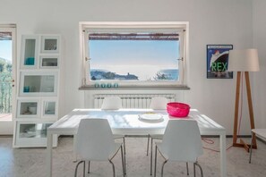 Un coin repas comprenant une table, des chaises, une fenêtre avec vue, un radiateur et une étagère avec des meubles de rangement dotés de portes en verre.