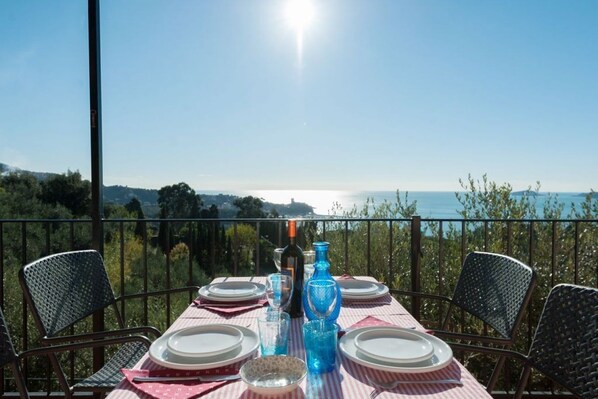 Une table dressée pour le dîner, avec vue sur la mer et les collines.