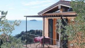 A balcony with a table and chairs, overlooking a coastal view. - Ulivi House: Parking, Pool, Tennis, 2 AC BDR, 2BTH, + Free Garage in Lerici LTZ! (Lerici)
