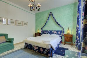 Une chambre à coucher avec un lit, un fauteuil vert, une table de chevet avec une lampe et une tête de lit à motifs floraux.