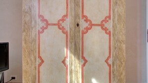 Quarto com um guarda-roupa de madeira grande e trabalhado, espelho e televisão sobre um suporte.