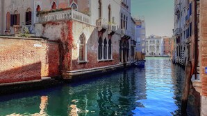 Um canal estreito com edifícios em ambos os lados, com janelas em arco e varandas.
