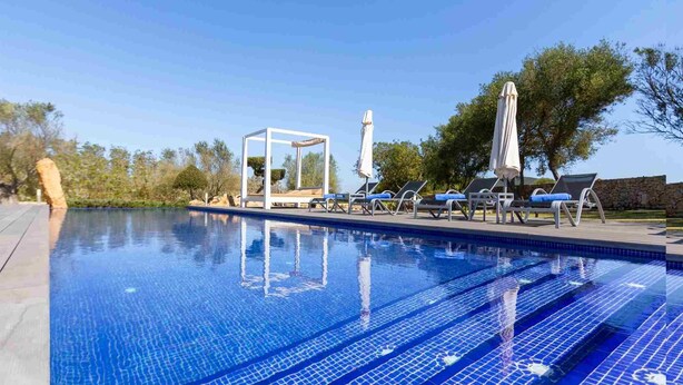 A clear blue pool with tiled steps, sun loungers, and a white pergola structure.