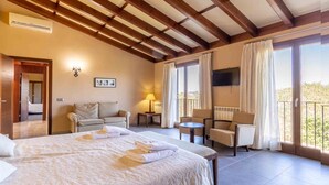 A hotel room with a large bed, a sofa, two armchairs, a TV, and a balcony with curtains.