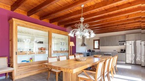A spacious kitchen with a wooden table and chairs, a large cabinet with glass doors, and a modern chandelier.