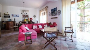 Una sala de estar con un sofá rojo, una mesa de centro de madera y un sillón de director. Hay una zona de comedor con una mesa y sillas, y una cocina con armarios y estufa.
