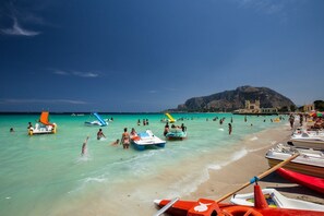 Una spiaggia con acque turchesi cristalline, persone che nuotano e si rilassano al sole, e diverse imbarcazioni.