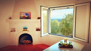 Ein Zimmer mit Kamin, einem Fenster mit Blick auf Bäume und Meer sowie einem kleinen Tisch mit Kerze und Flasche.