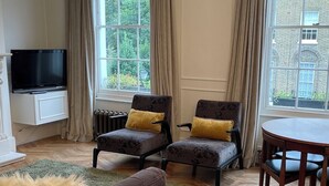 A living room with a flat-screen TV, two armchairs with cushions, a round wooden table, and a green rug. - Stylish in Angel, by Veeve (London)