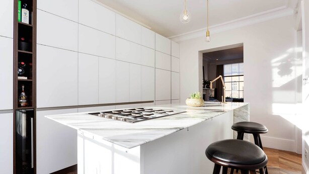 A modern kitchen with a marble island, two stools, a built-in wine rack, and pendant lighting. - Stylish in Angel, by Veeve (London)