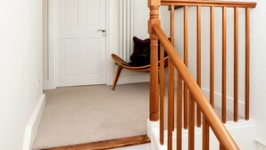 A staircase with wooden steps and a wooden handrail, leading to a white door with a mirror above it. - Stylish in Angel, by Veeve (London)