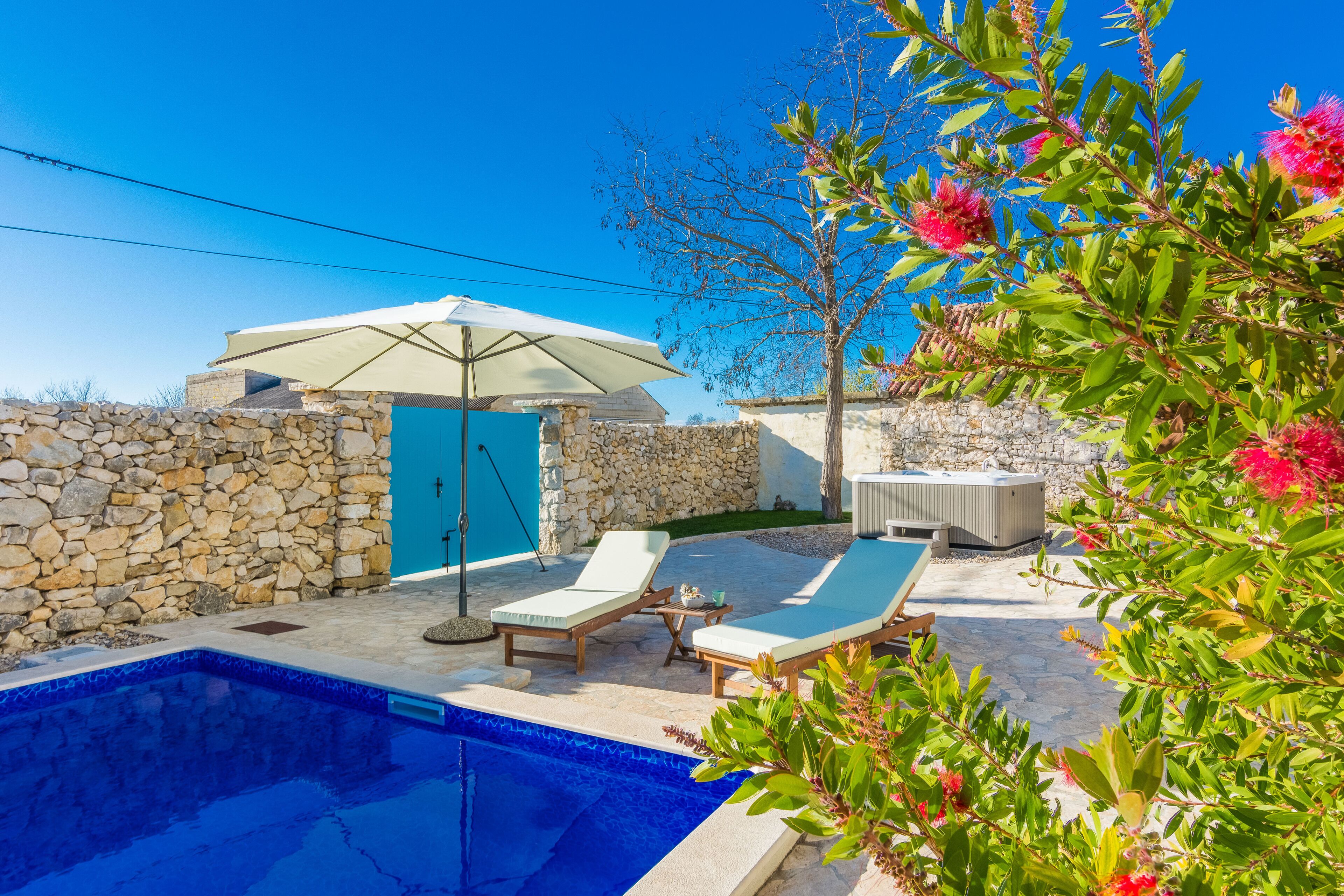 A pool area with lounge chairs, a stone wall, and a blue door.