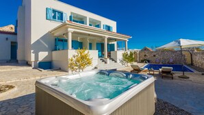 A modern villa with a hot tub, outdoor seating, and a swimming pool.