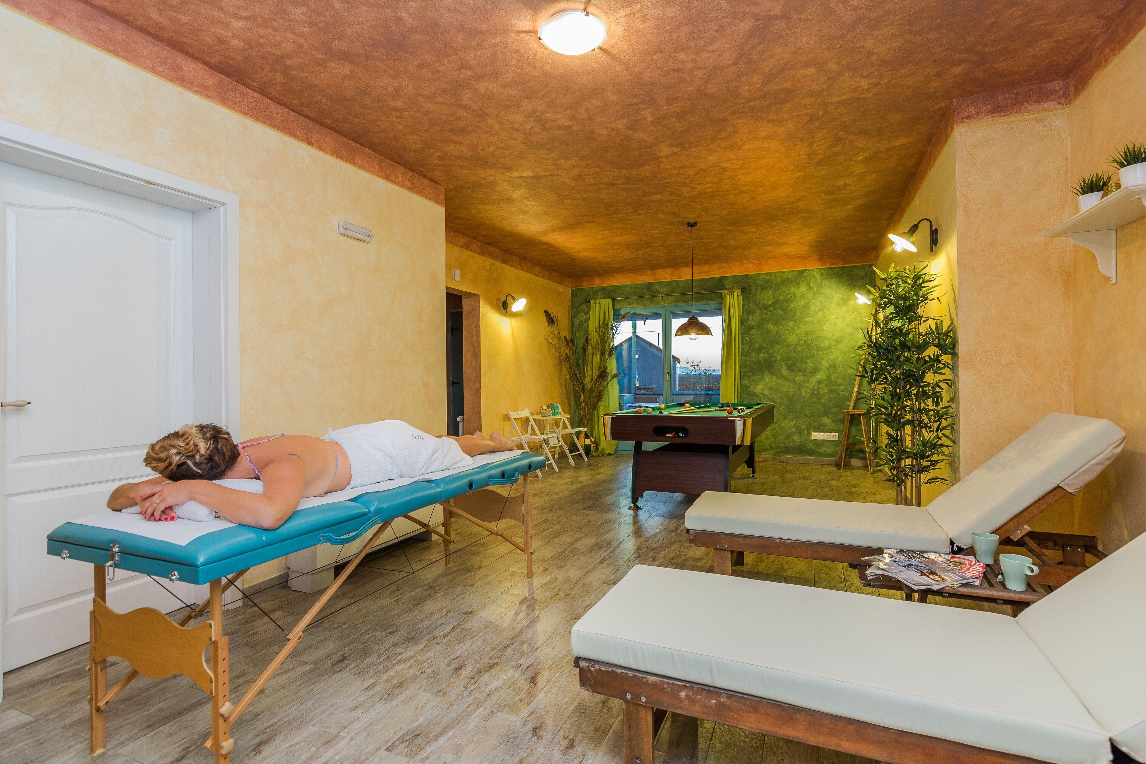 A room with a massage table, two lounge chairs, a pool table, and a door.