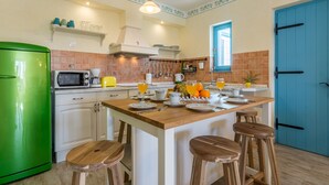 A kitchen with a green refrigerator, a wooden island with stools, and a blue door.