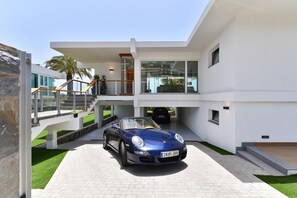 Uma casa moderna de dois andares com um Porsche conversível estacionado na entrada.