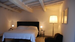 Un dormitorio con una cama grande, dos lámparas de noche, una mesita y una silla.
