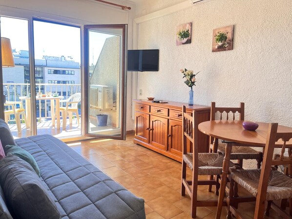 A living room with a sofa, wooden dining table, chairs, and a TV.