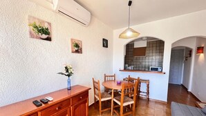 A dining area with a wooden table and chairs, a vase with flowers, and a kitchen visible through an archway. - 0168-POBLAT TIPIC Studio near the beach (Empuriabrava)