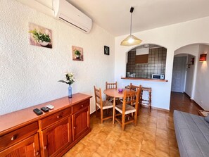 A dining area with a wooden table and chairs, a vase with flowers, and a kitchen visible through an archway. - 0168-POBLAT TIPIC Studio near the beach (Empuriabrava)