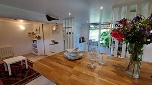 A modern kitchen with a wooden dining table, white cabinets, and a view of the garden through a glass door.