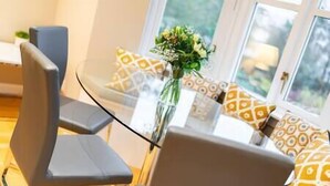 Een moderne eethoek met een glazen tafel, grijze stoelen en gekleurde kussens.