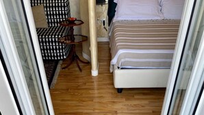 Une pièce avec un lit, un canapé et une petite table. Le sol est en bois et il y a un tapis vert sur lequel est écrit « bienvenue chez vous ».