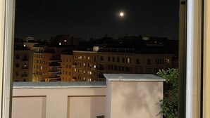 Un balcon offrant une vue sur un paysage urbain nocturne, avec des bâtiments et la lune.